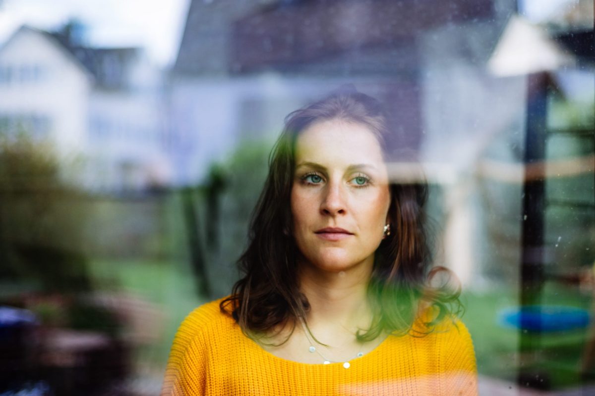 sexual-abuse-survivor-staing-out-window A forlong looking young woman in a bright sweater stares out a window, deep in thought