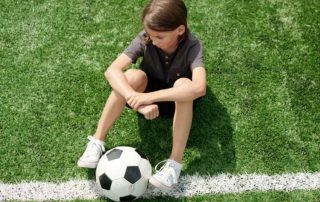 Young child sitting alone on a soccer filed with a soccer ball