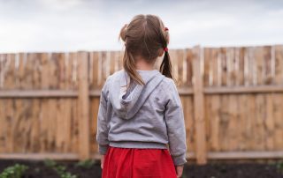The back of a young girl with pigtails who is looking at fence in a yard