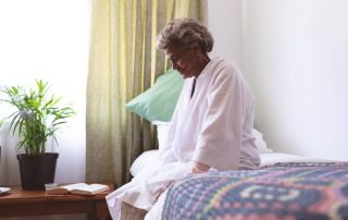 An African American older woman sitting on a bed looking at the ground