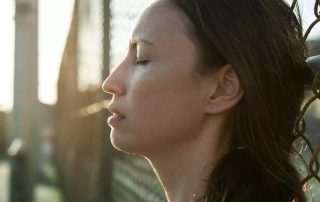 A woman with her eyes closed leaning against a chain linked fence
