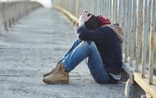 A young male sitting on a bridge with his heads in his hands