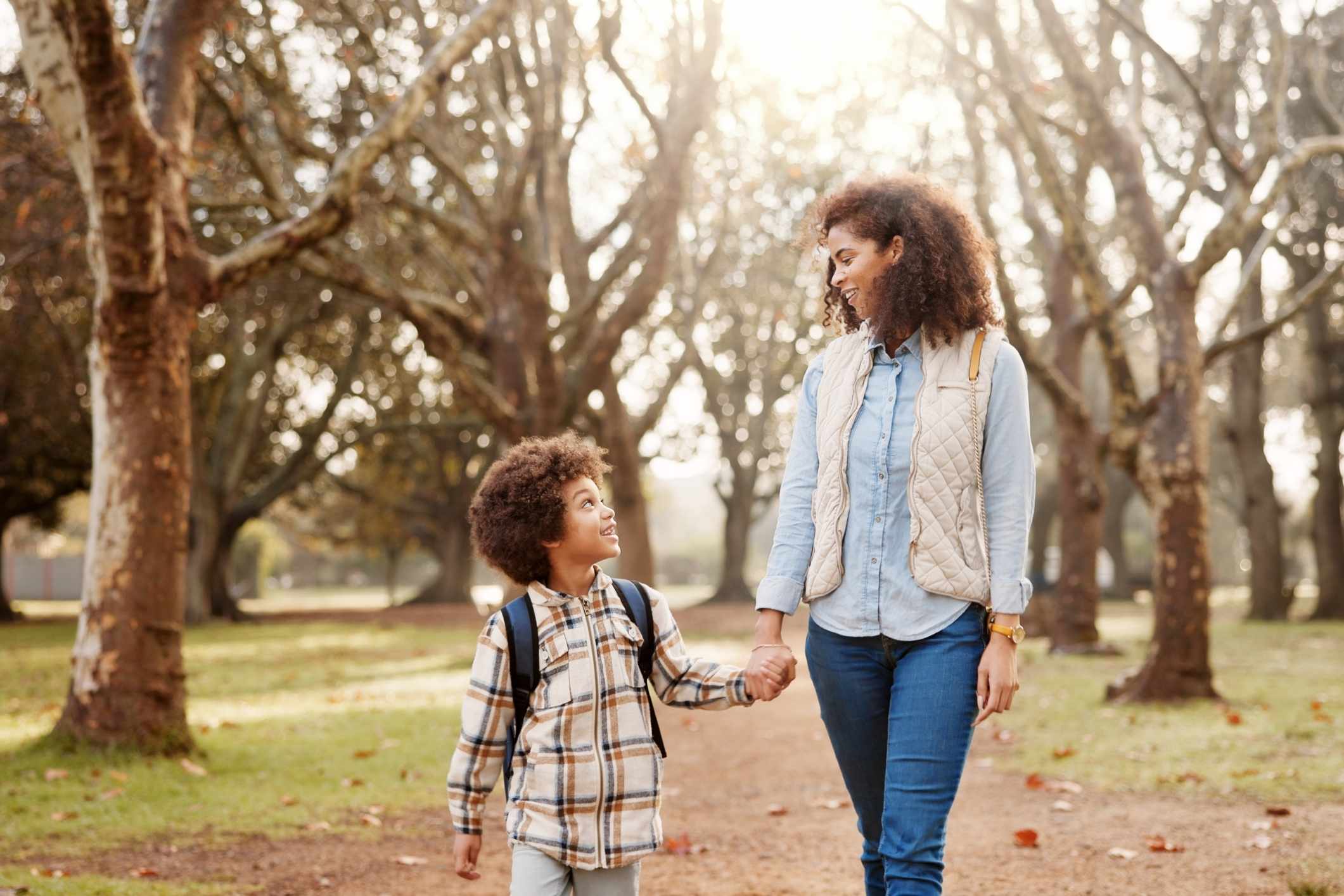 67ec41a474db50139d7589e8_Mother20talks20to20her20son An African American woman walking and holding hands with a young Aftican Americn boy in an outdoor park setting