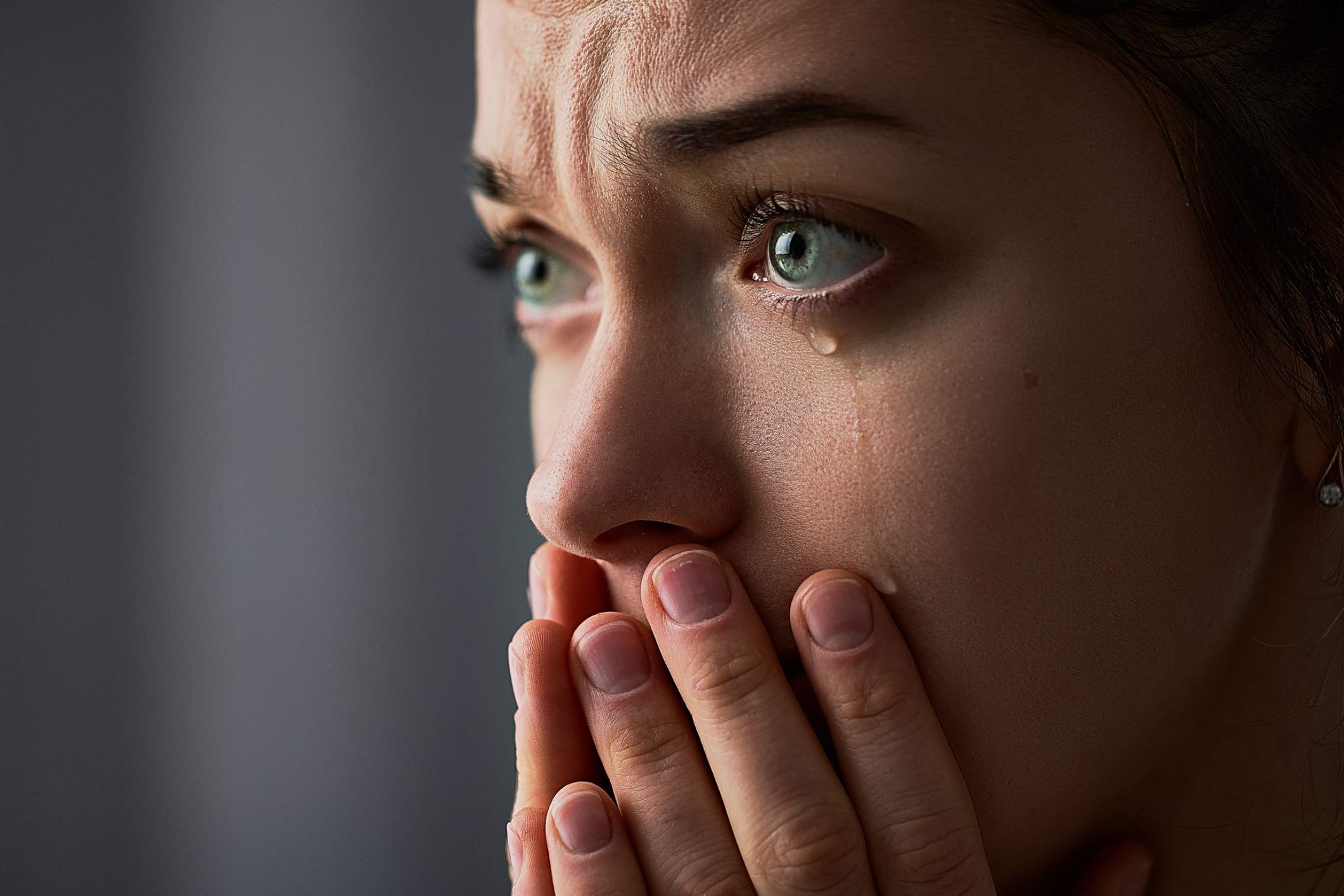 Close up of a woman's face with her hands covering her mouth with tears falling from her eyes