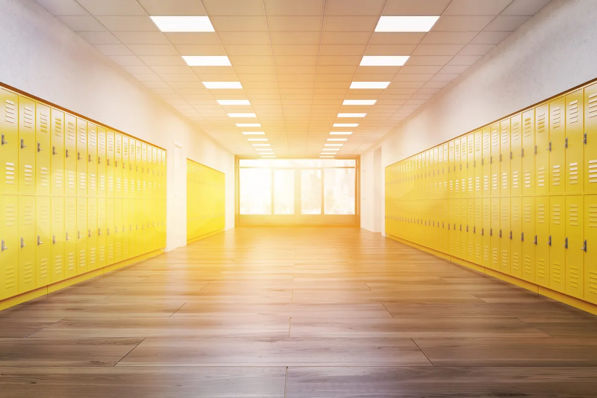 Empty school corridor with bright yellow lockers and the sun shining through doors.