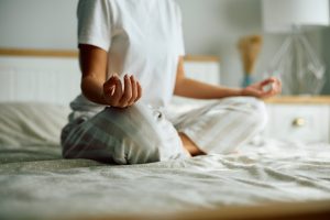A woman sitting in bed at home meditating.