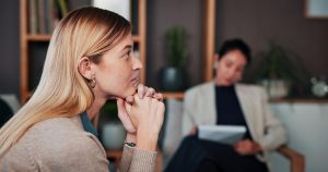 Female attorney sitting on a couch and taking notes while consulting with a female client in deep thought.