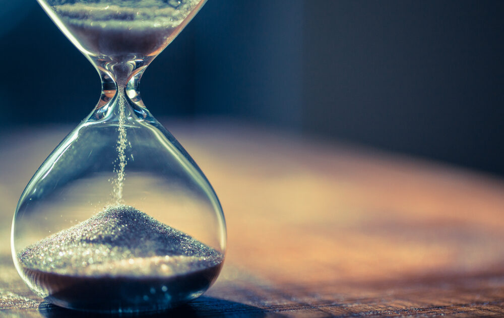 Sand slowly pours through an hourglass, indicating the passage of time.